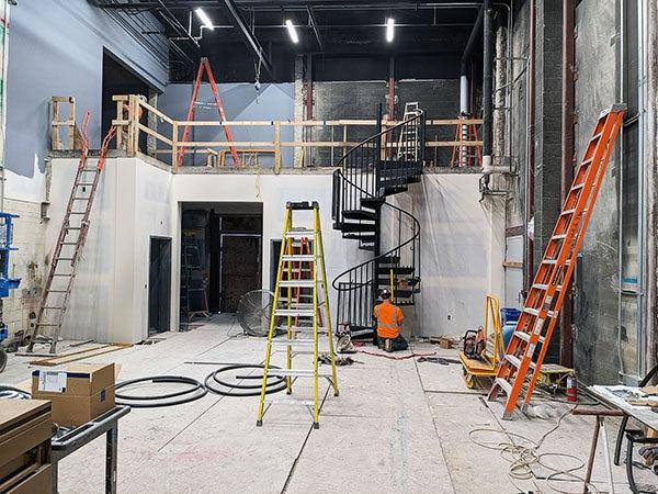 a black metal spiral staircase goes from the floor level to raised area under construction