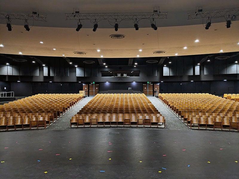 a view out into a auditorium with rows of light colored seats with dark walls, doors, and a control booth on the back wall